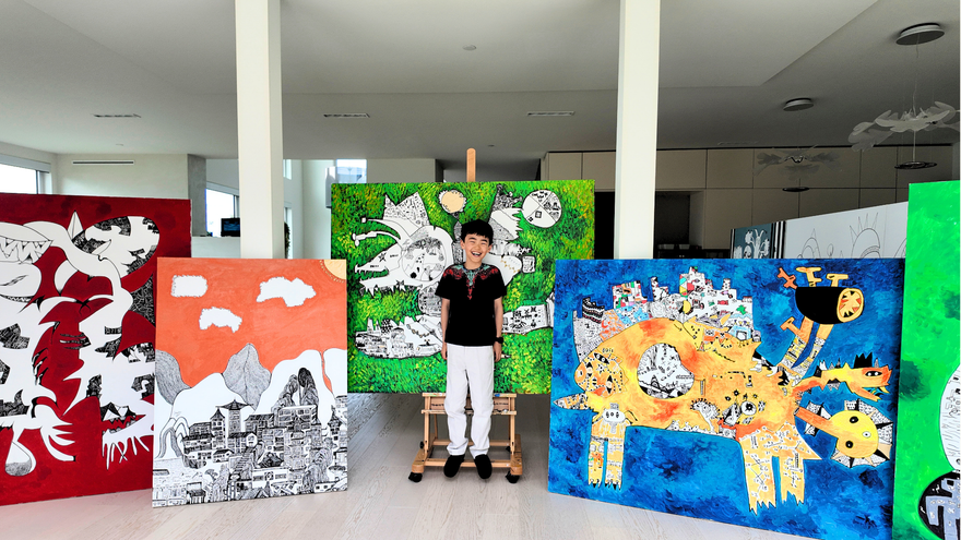 Young artist Jayden Ju stands smiling among several of his large-scale colorful paintings in a bright contemporary studio, showcasing his vibrant, imaginative artworks featuring abstract landscapes, fantastical creatures, and graphic illustrations.