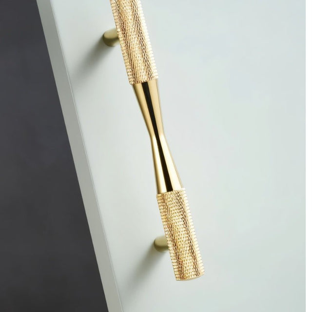 "A close-up of a brass pull bar handle with a knurled texture and sleek, modern design, mounted on a white surface."