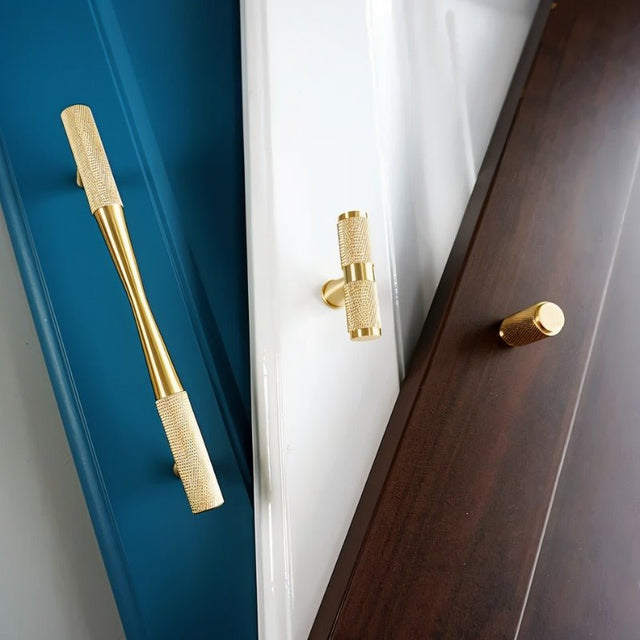 "A variety of brass door hardware, including a long pull bar and two shorter handles with knurled detailing, mounted on different colored doors."