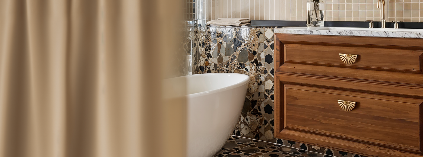 Bathroom with a freestanding bathtub, wooden vanity featuring the Flaro brass pulls, and mosaic tile wall.