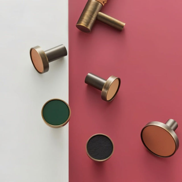 "Modern brass and leather cabinet knobs in green, tan, and black on a red and white background."
