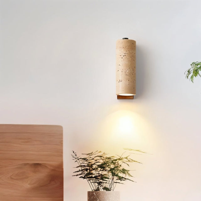 "Travertine wall lamp with a cylindrical shade and wooden base, providing soft lighting in a modern bedroom setting."
