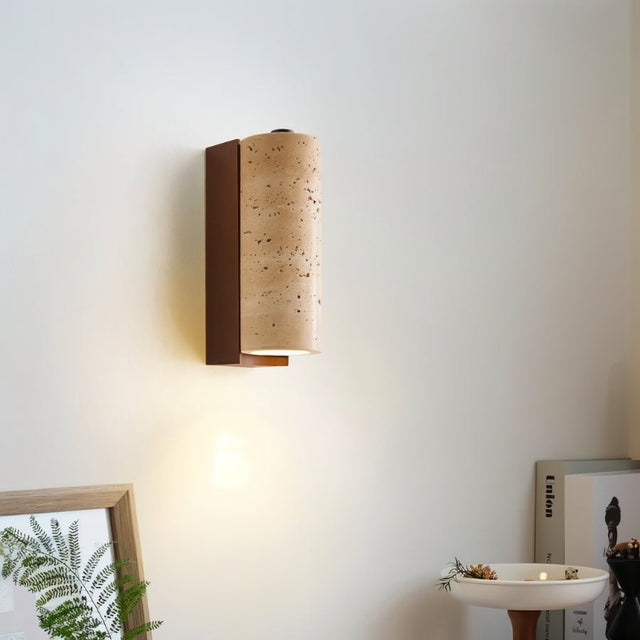 "Wall-mounted lamp with a cylindrical travertine shade and wood base, emitting a soft glow in a modern room."