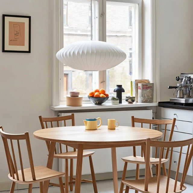 "Modern pendant light illuminating a cozy dining area with wooden chairs and table, minimalist decor by a window."