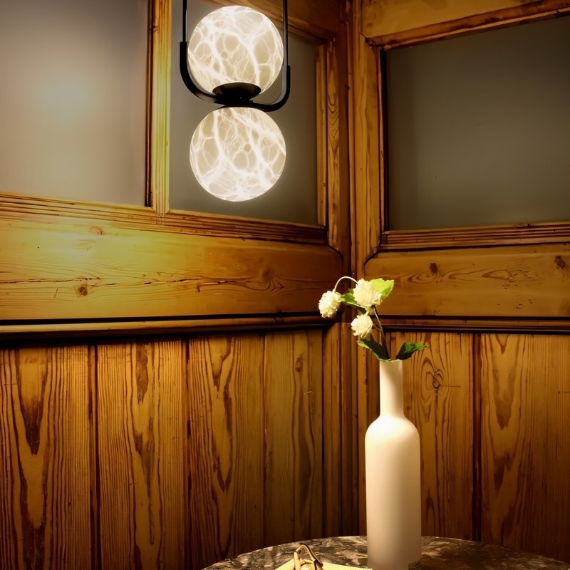 "Elegant pendant lamp made from alabaster and aluminum, casting a warm glow in a cozy room with wooden walls and a minimalist vase, perfect for enhancing contemporary interiors."