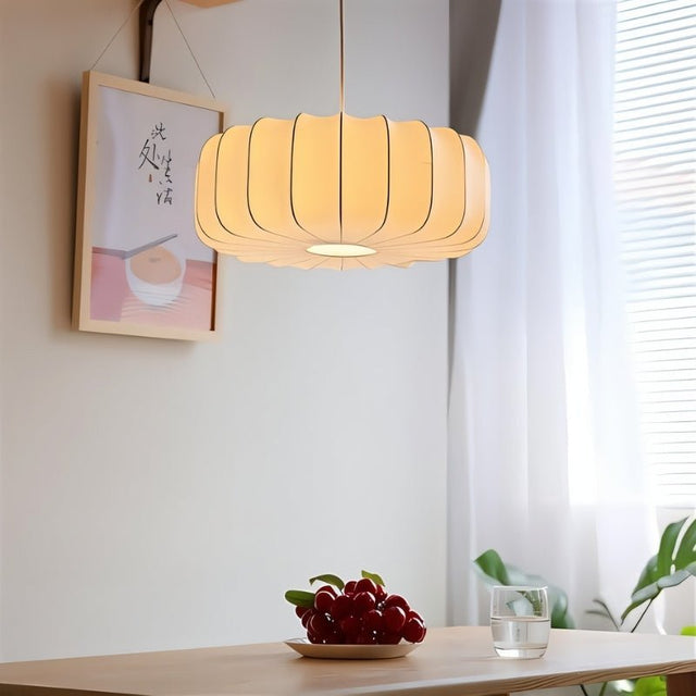"Elegant pendant light with a pleated iron and silk design, softly illuminating a dining table with a warm, inviting glow."
