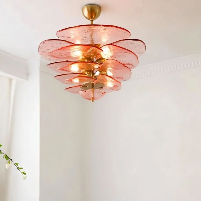 "A pink Murano glass chandelier with layered petals, hanging in a room with white walls and a plant."