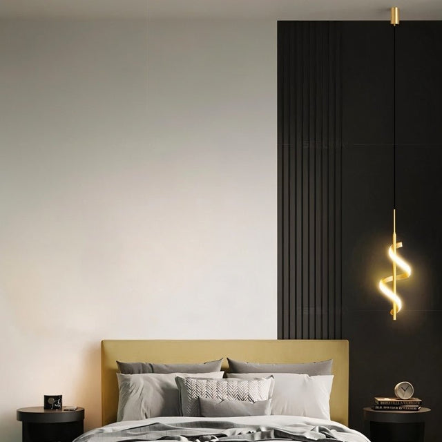 "A gold pendant light with a spiral design, shown lit up next to a bed with a gold headboard and gray pillows, in a room with a white wall and a black wall with vertical grooves."