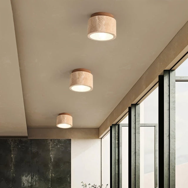 "Three cylindrical yellow travertine ceiling lights with dark wood tops in a room with large windows, modern interior lighting."