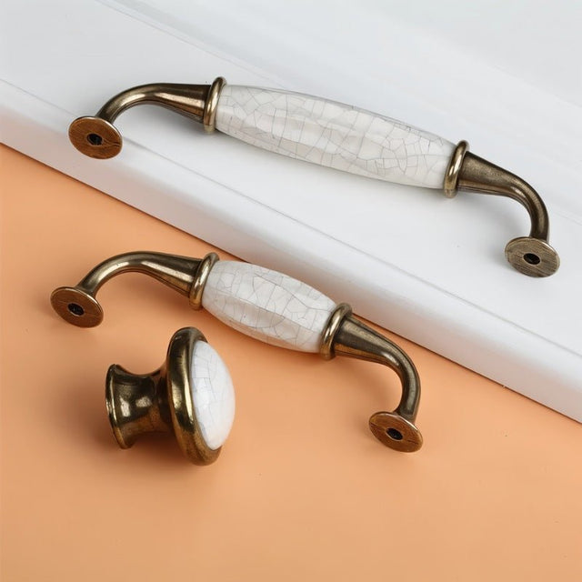 "Pair of ceramic pull bar handles with a crackled glaze and antique brass finish, alongside a matching knob."