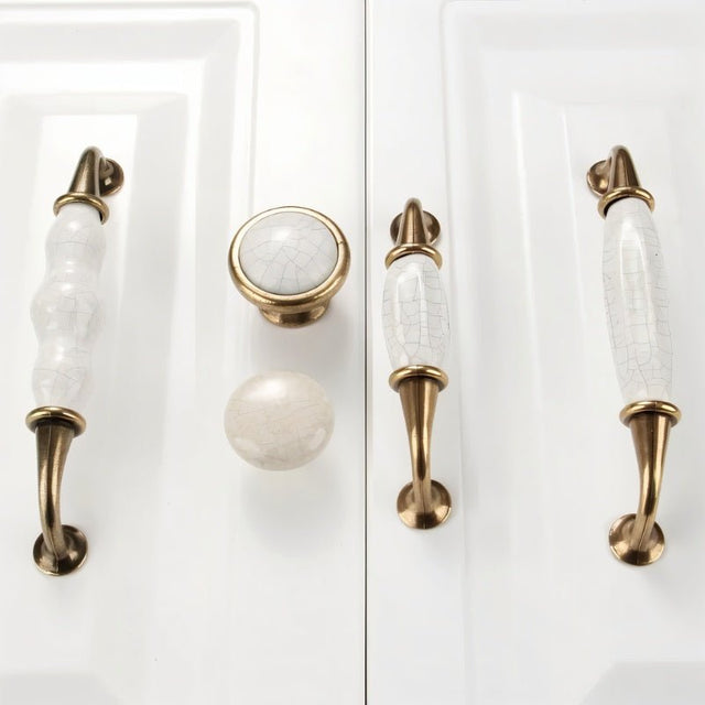 "Ceramic pull bar handles and matching knobs with a crackled glaze and antique brass finish on white shaker-style cabinet doors."