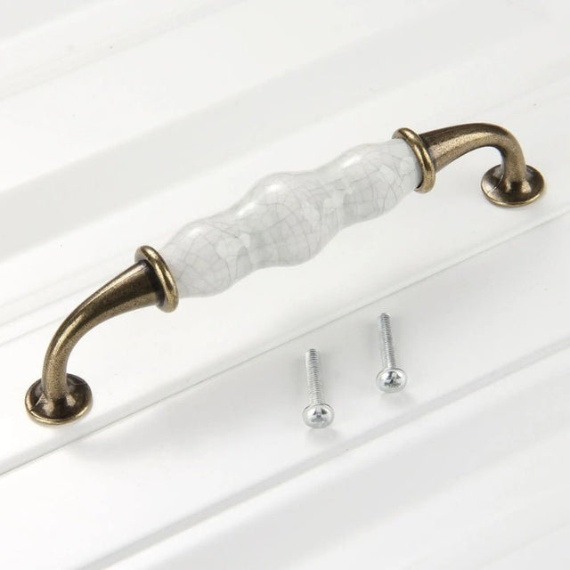 "Ceramic and brass pull bar with a crackled glaze, antique brass finish, and two screws on a white surface."