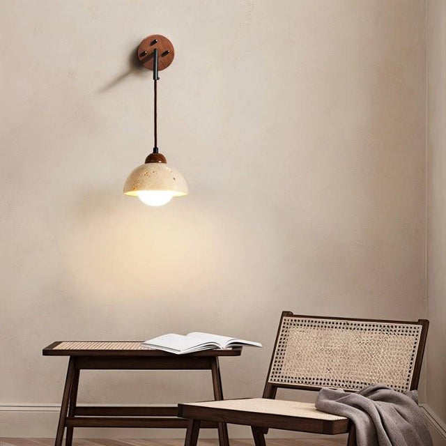 "A modern wall lamp with a dome-shaped yellow travertine shade and a wooden mount, casting a warm, ambient light in a cozy bedroom nook."