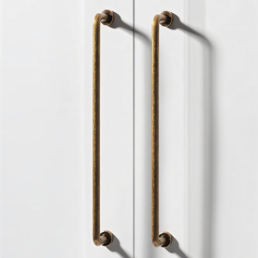"Two long, minimalist antique brass pull bar handles made of durable zinc, installed on white doors, featuring a slim, cylindrical design with rounded ends."