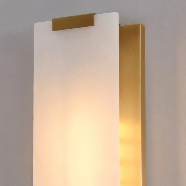"Detail of a modern wall lamp showing a rectangular alabaster panel with soft, warm light glowing through it and a brass accent at the top."