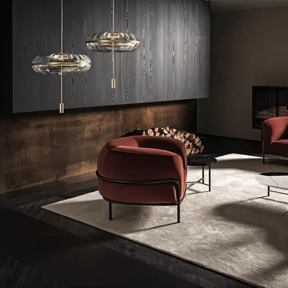 "Two sculptural glass pendant lights with rippled texture and metal frames, hanging above a living room with armchairs and a rug."