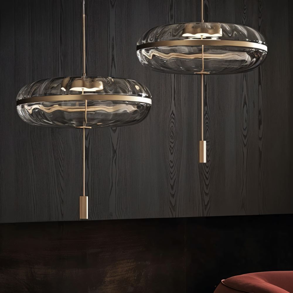 "Pair of sculptural glass pendant lights with rippled texture and metal frames, hanging in a room with dark walls."