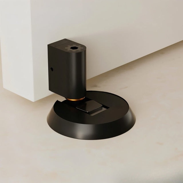 "Black brass door stop installed on a floor next to a white door."