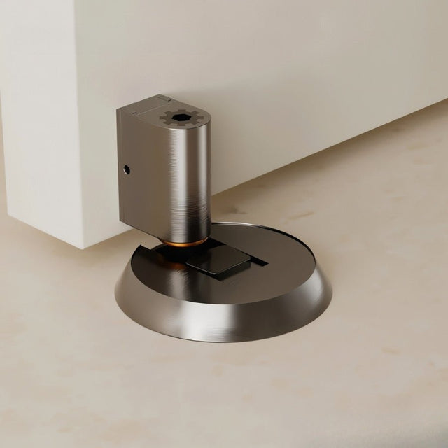 "Silver brass door stop installed on a floor next to a white door."