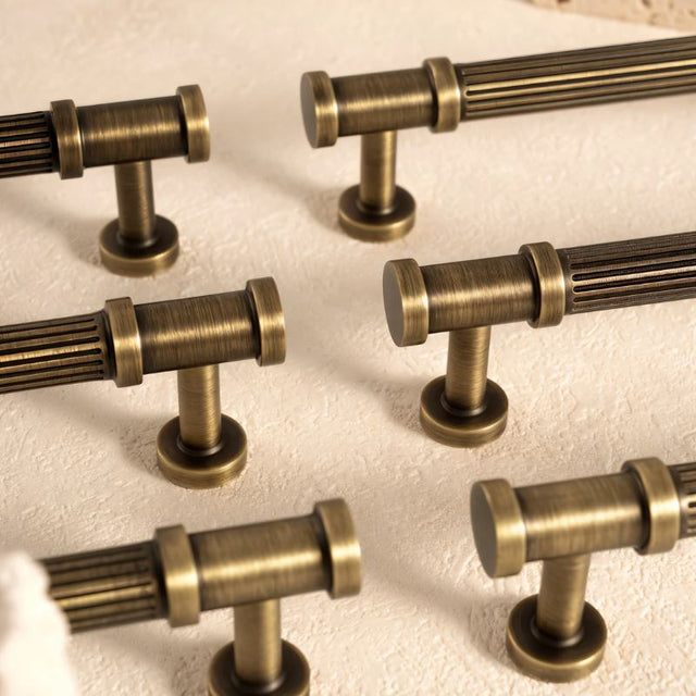 "Close-up of antique brass fluted knobs and pull bars with detailed end caps, showcasing a ribbed texture and classical charm."