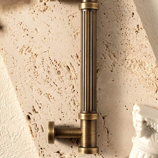 "Close-up of an antique brass fluted pull bar with detailed end caps on a textured background, highlighting its ribbed design and classical charm."