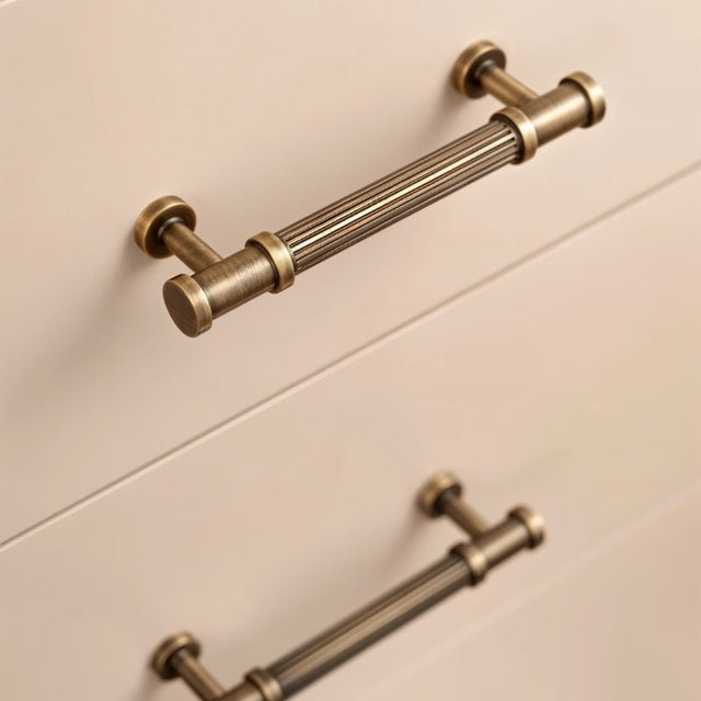 "Antique brass fluted pull bars with detailed end caps on drawers, adding classical charm to a space."