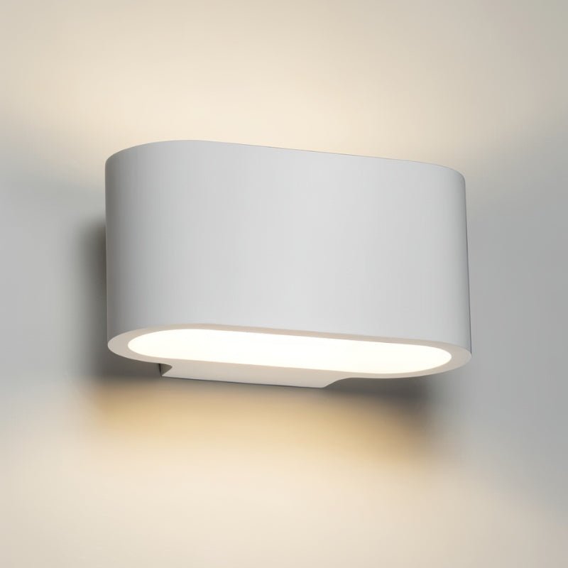 "Front view of a white gypsum Arcat wall lamp with a rounded rectangular shape, emitting soft uplighting and downlighting on a light gray wall."