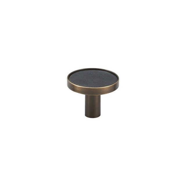 "A modern black leather and brass cabinet knob on a white background."