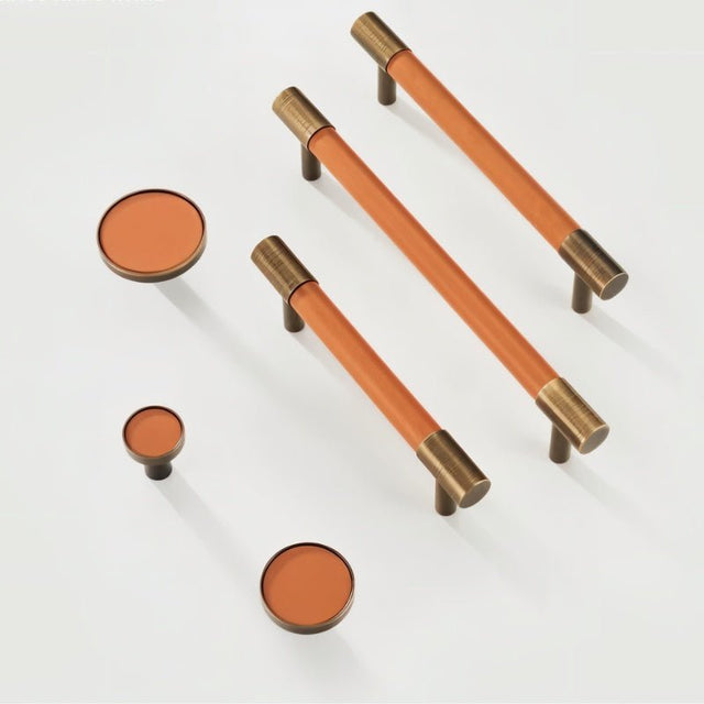 "Modern tan leather and brass pull bars and knobs for cabinets on a white background."