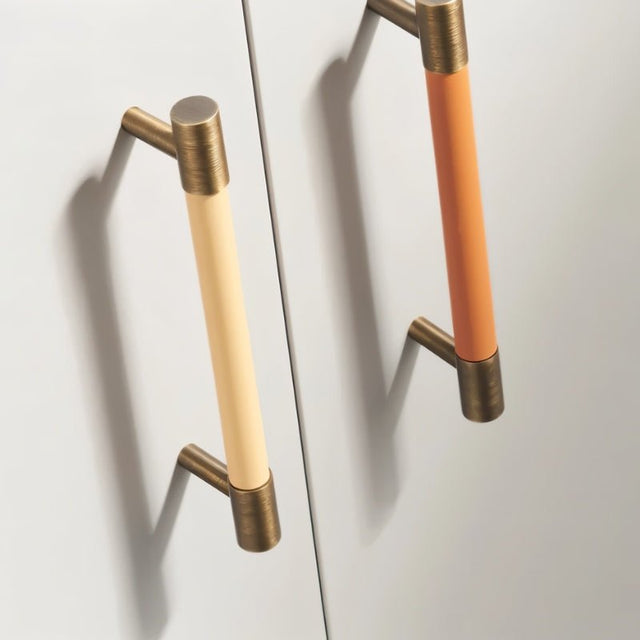 "Modern tan and orange leather and brass pull bars on a white cabinet."