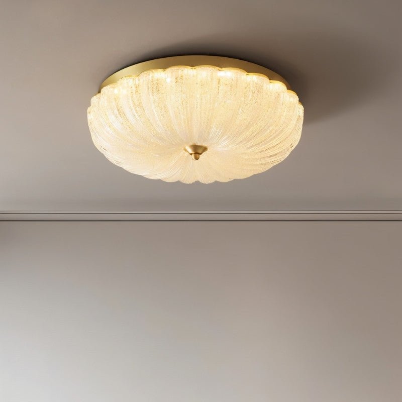 "A modern glass ceiling light with a brass frame, illuminated against a gray background."