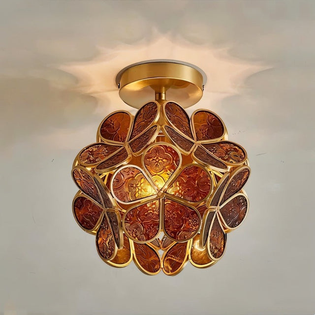 "A close-up of an amber, floral-inspired ceiling light with a brass frame and textured glass petals, showcasing its intricate details and warm glow."