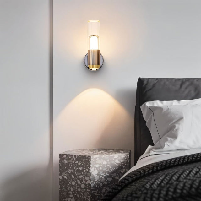 "Modern cylindrical wall lamp with a metal base and acrylic diffuser providing ambient light in a bedroom."