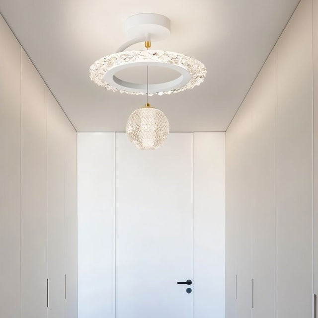 "A white ceiling light with a circular frame and a hanging crystal sphere, installed in a white hallway."