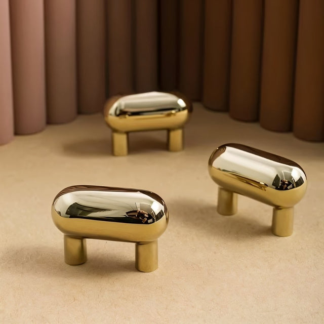 "Group of sleek, capsule-shaped brass knobs on a light surface with a backdrop of varying neutral tones."