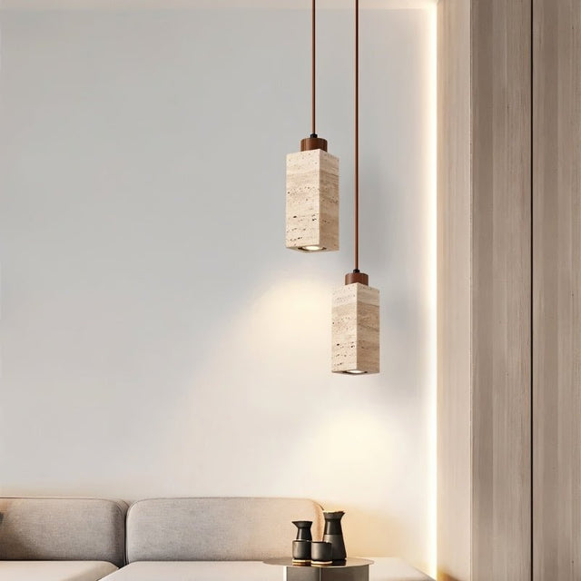 "Pair of modern minimalist pendant lights with rectangular travertine bodies, adding a touch of rustic charm to a contemporary living room."