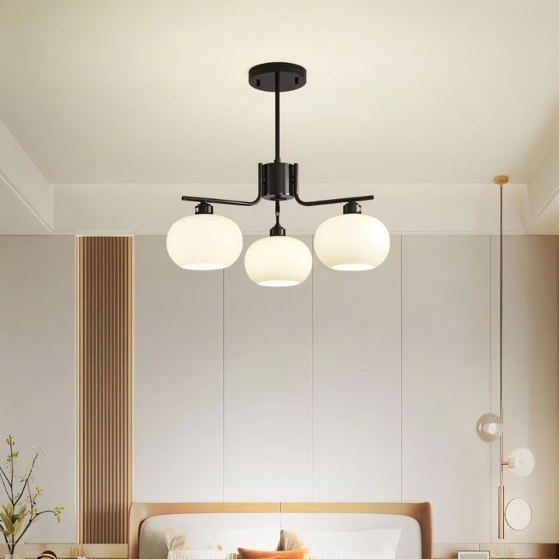 "A 3-light round chandelier with opal glass globes and a black metal frame, hanging in a modern bedroom with a bed and decor."