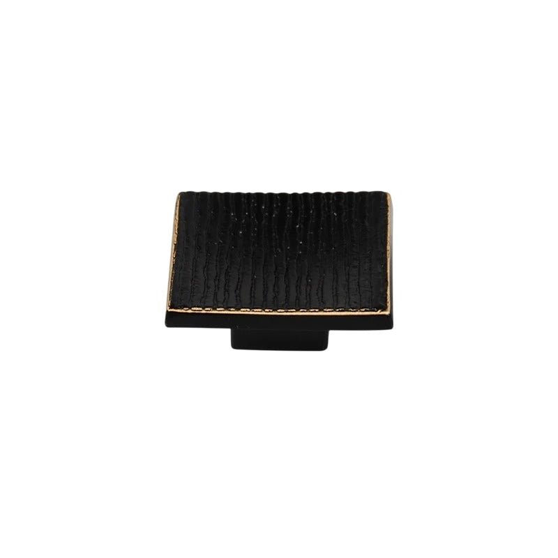 "Studio shot of a single black square cabinet knob with a ridged, textured surface on a white background."