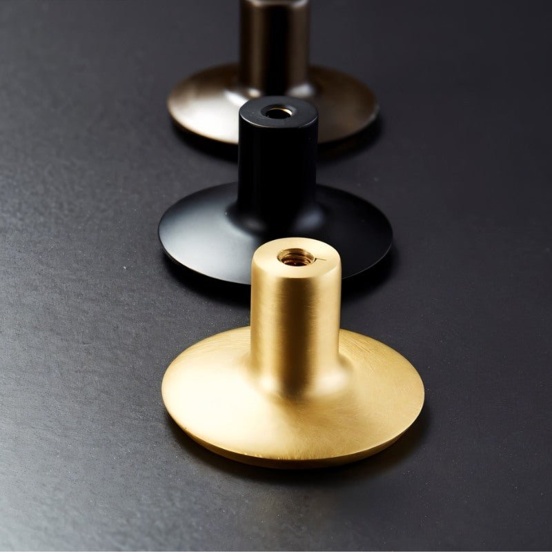 "Back view of three circular brass knobs in gold, black, and bronze with visible screw threading."