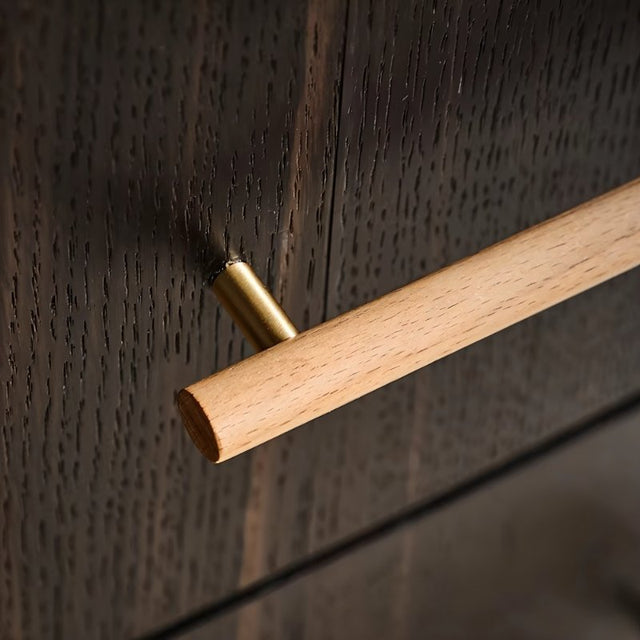 "Close-up of a wooden drawer pull with brass detailing on a dark wood surface."