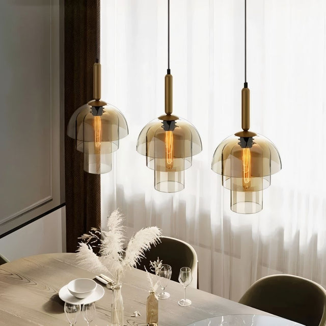 "Three modern pendant lights with layered smoked glass shades and metallic accents over a dining table."