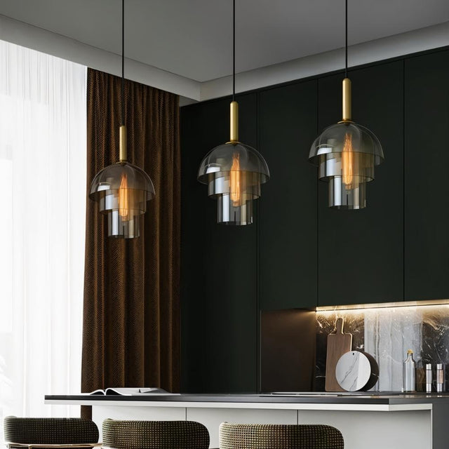 "Three modern pendant lights with layered smoked glass shades and metallic accents over a kitchen island."