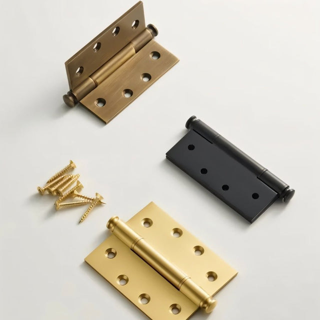 "Top view of three solid brass barrel hinges with decorative finials in antique, black, and polished finishes, shown with screws on a light background."
