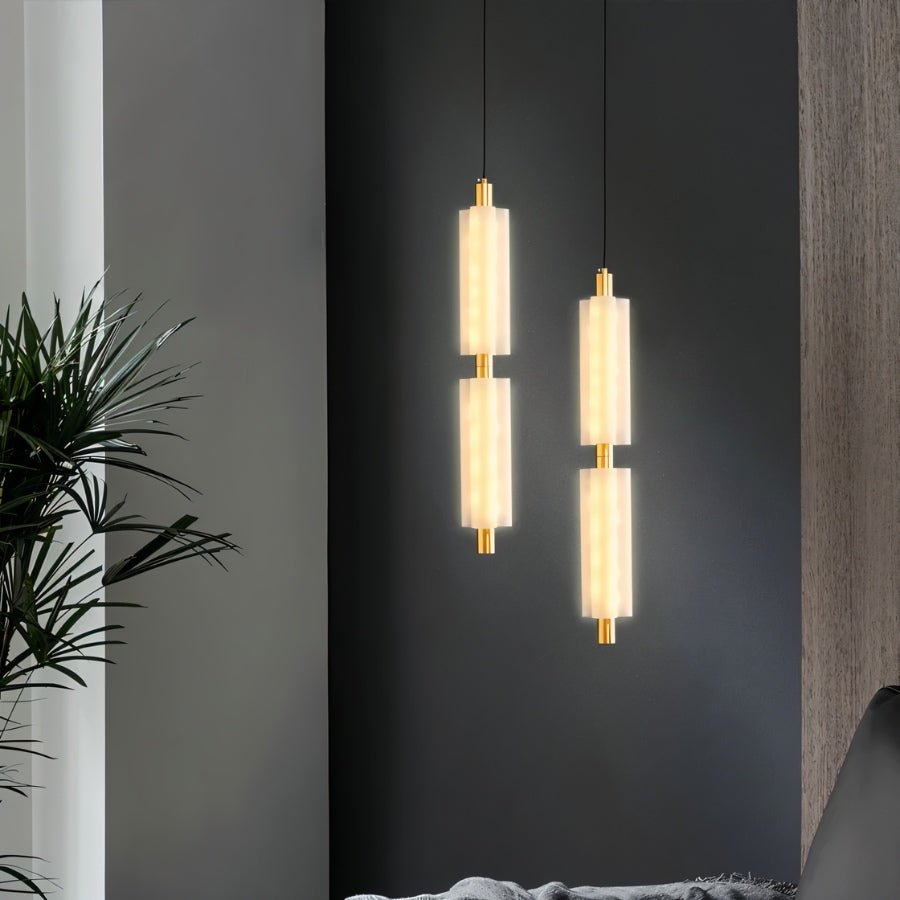 "Two minimalist pendant lights with frosted acrylic and brass, illuminating a modern living room with a gray accent wall."