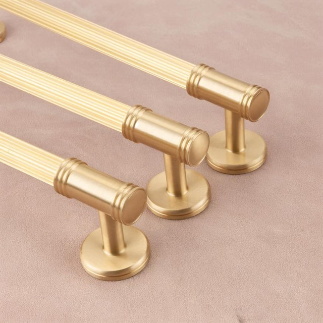 "Close-up lifestyle image of sleek brass pull bars with grooved detailing, showcasing a sophisticated and timeless design on a neutral surface."