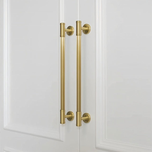 "Two sleek brass pull bars with grooved detailing mounted on white wardrobe doors, showcasing a sophisticated and timeless design."