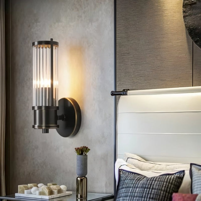 "A modern wall lamp with clear glass panels in a bedroom setting, mounted on the wall beside a bed."