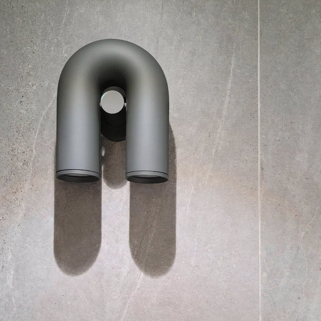 "A gray, contemporary wall lamp with a looped design, mounted on a textured gray wall, casting a soft light and shadow."