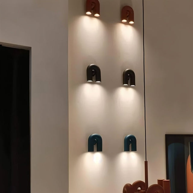 "Multiple contemporary wall lamps in red, black, and blue, arranged in a vertical row on a white wall, showcasing a unique, looped design and adjustable lighting."