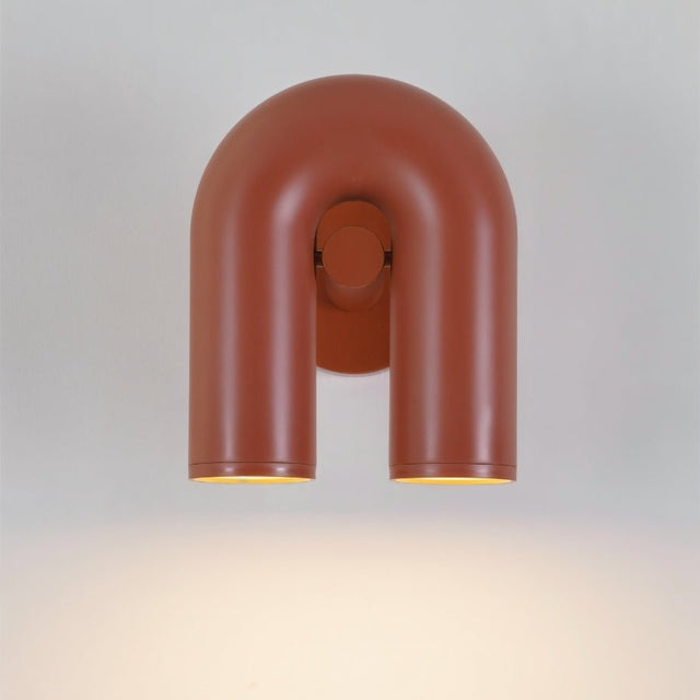 "A front view of a red, contemporary wall lamp with a looped design, showing its dual light sources illuminated against a white background."
